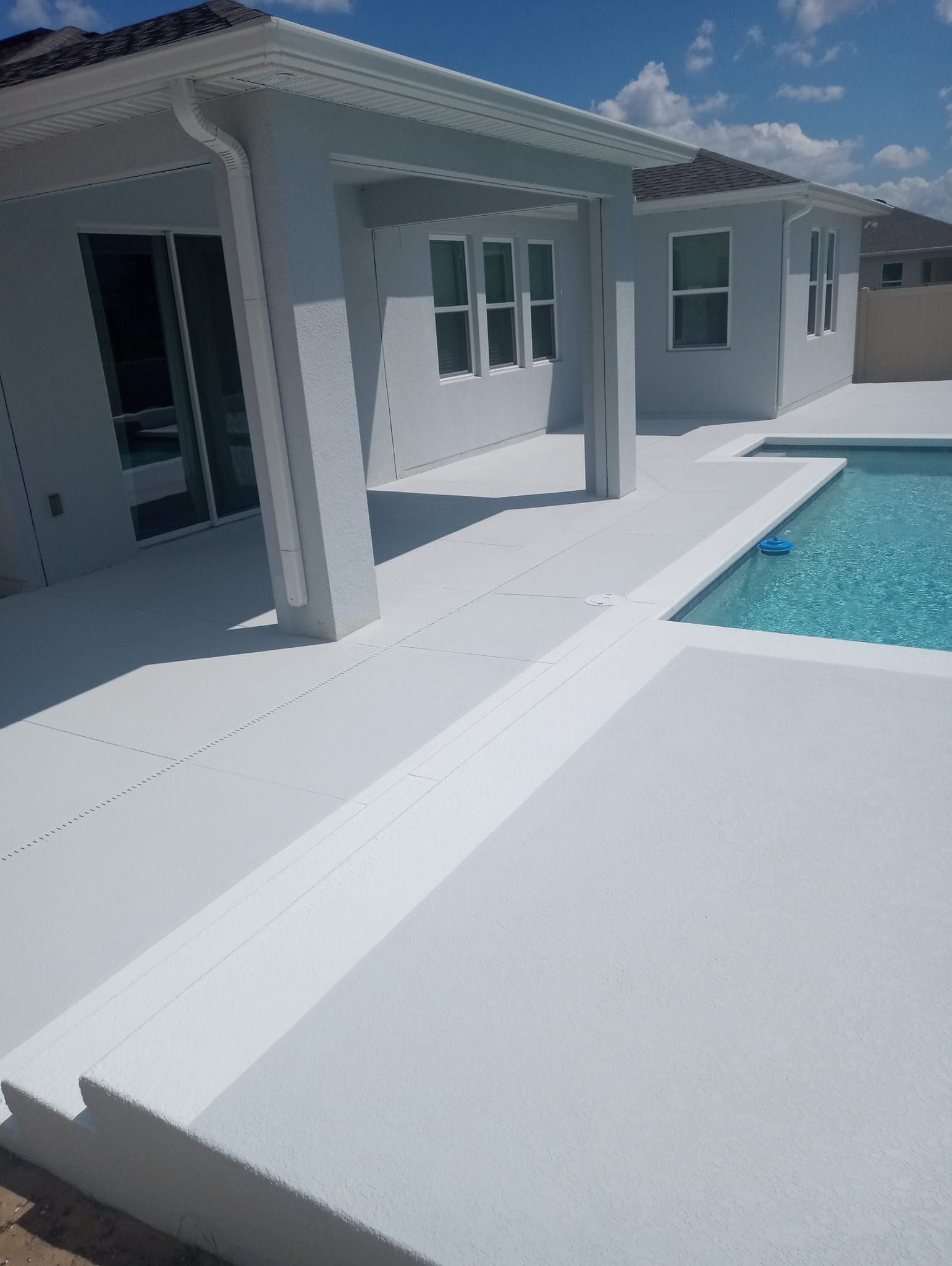Modern white house patio beside a turquoise swimming pool under bright sunlight
