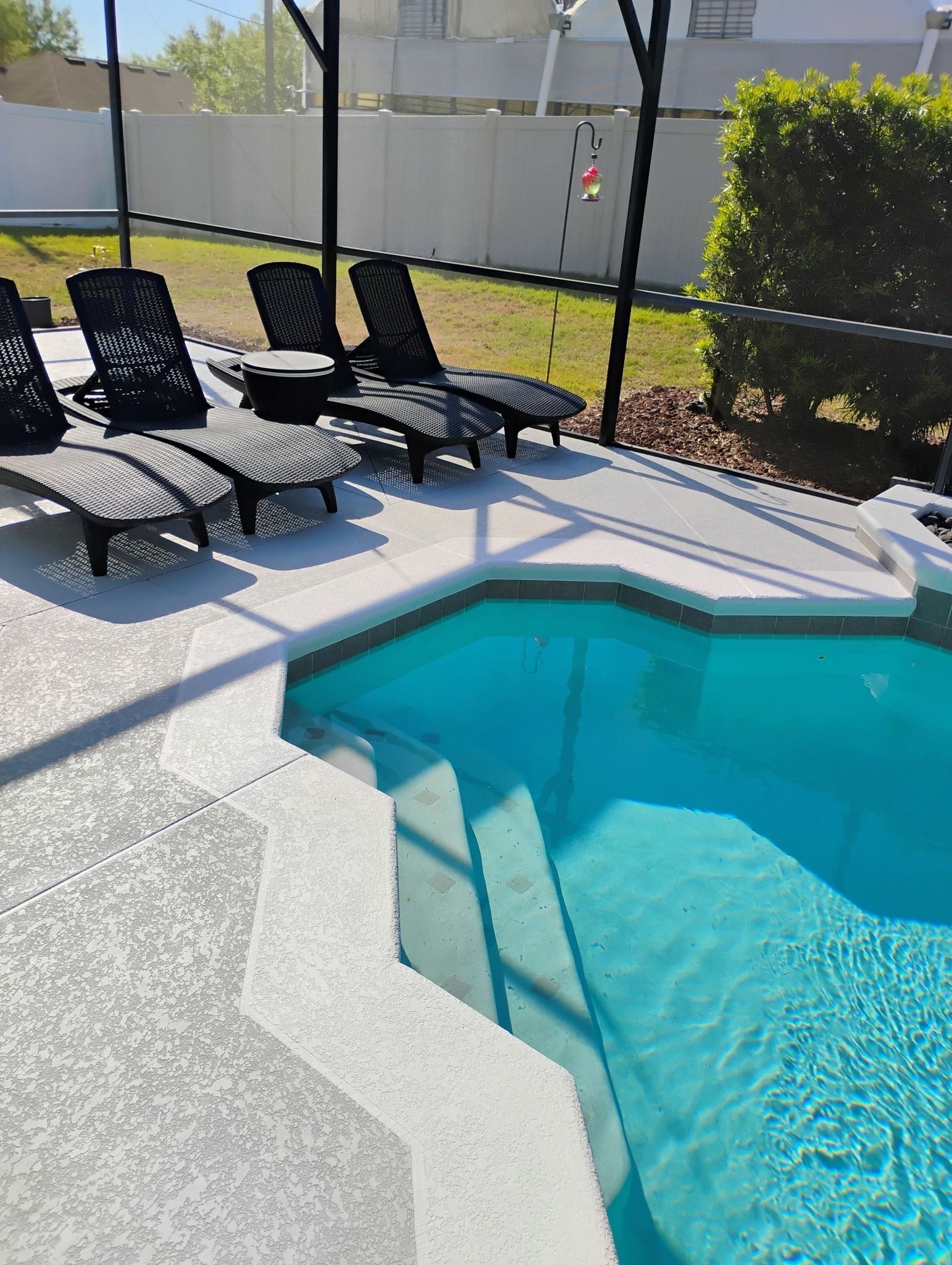 Poolside lounge chairs beside a turquoise swimming pool under a screened enclosure.