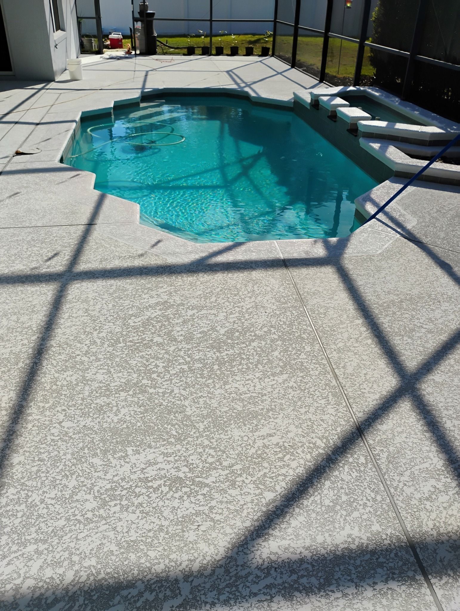 Screened backyard pool with turquoise water, white deck, and lounge chairs in bright sunlight