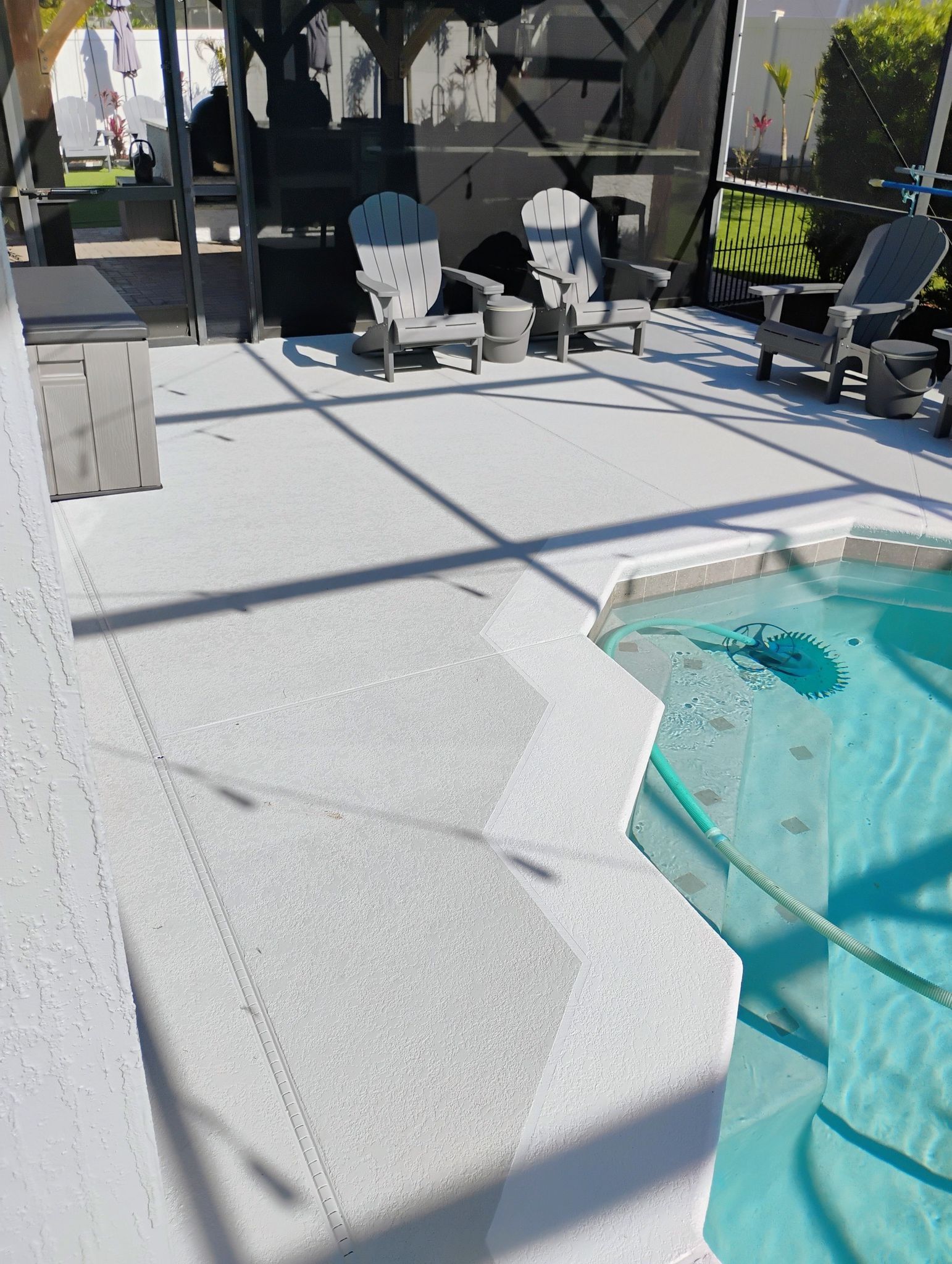 Backyard pool deck with turquoise water, white chairs, grill, and palm tree shadows