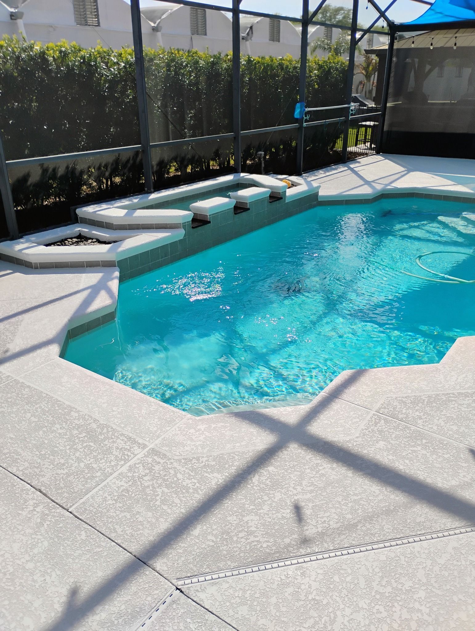 Pool deck resurfacing surrounding a screened-in residential swimming pool with a light gray textured finish, built-in seating, and clear blue water.