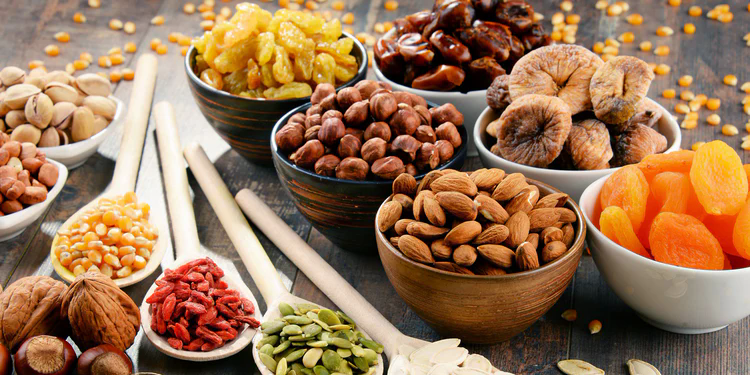 A variety of dried fruits and nuts in bowls and spoons on a wooden table.