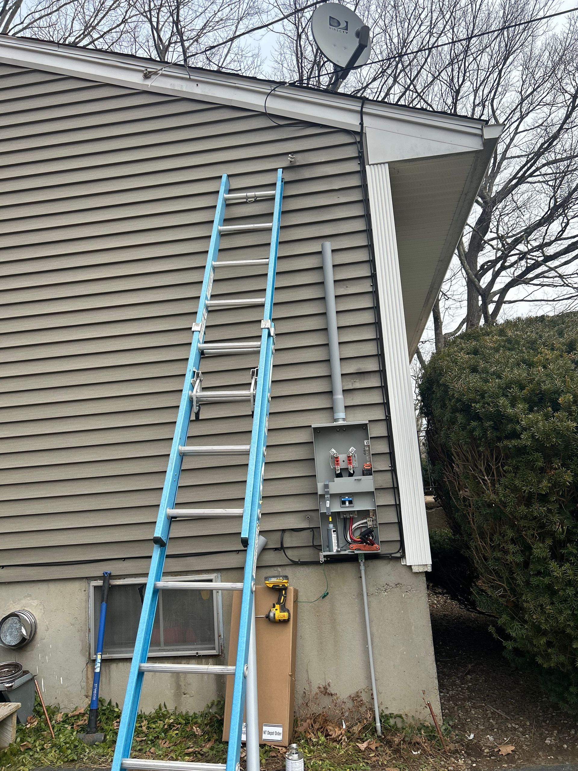 A blue ladder leans against a tan-sided house near an electrical box and a satellite dish.