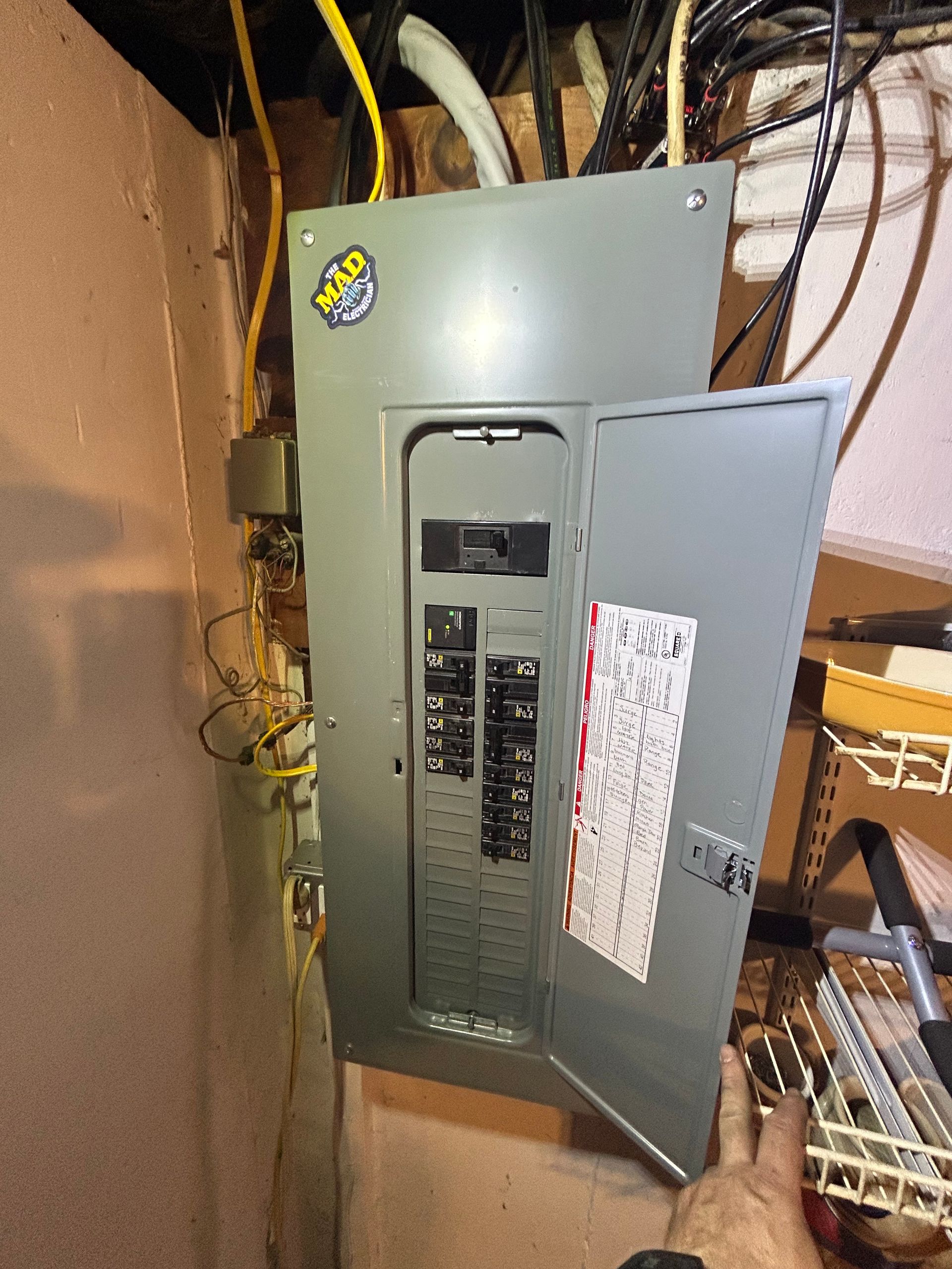 Electrical panel with open door in a basement, showing circuit breakers and wiring.
