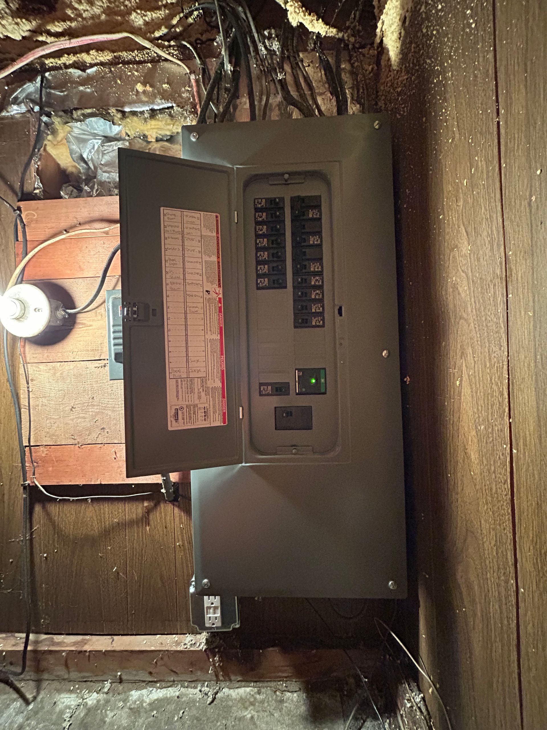 A black electrical box is hanging on a wooden wall.