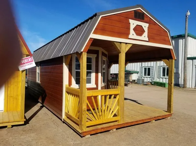 Red and yellow cabin with a porch, set outdoors on a sunny day.