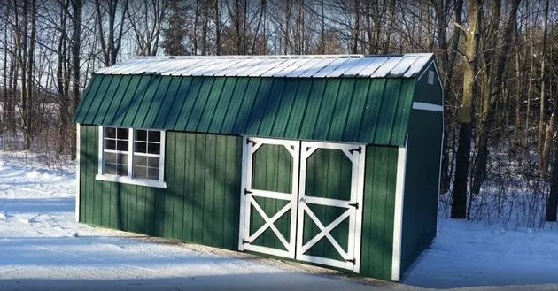 Green shed with white-trimmed double doors and window, snow on roof and ground, winter scene.