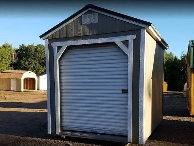 Small, grey storage shed with roll-up door; white trim and a light blue sky in the background.