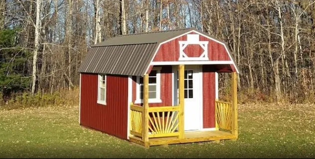 Red shed with a small porch on grassy ground, surrounded by trees.
