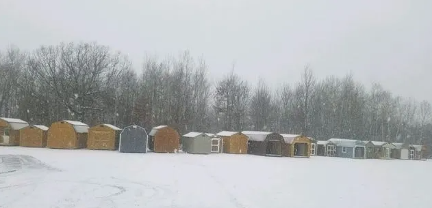 Snowy landscape with a line of ice fishing huts. Trees in the background.