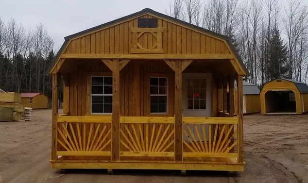 Wooden cabin with porch, two windows, door, and decorative sunburst railing.