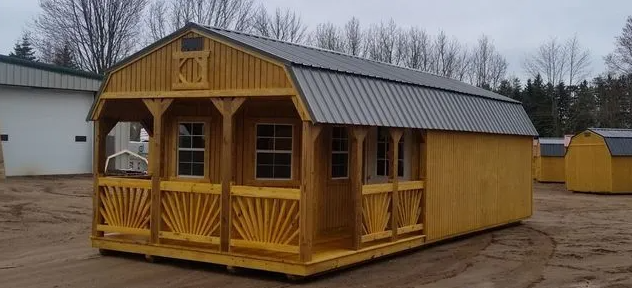 Wooden cabin with porch and metal roof, set in a field with other sheds.