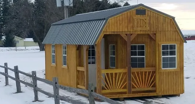 Wooden shed with a porch, grey roof, and windows, surrounded by snow.