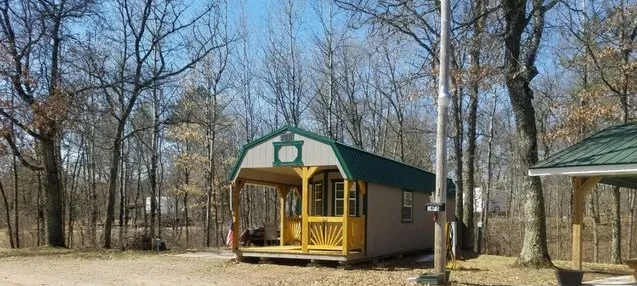 A small cabin with a porch, surrounded by trees under a blue sky.