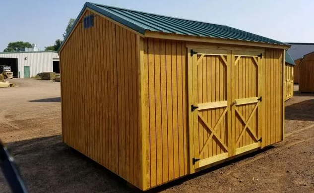 Wooden shed with green metal roof, double doors, and yellow siding, outdoors.