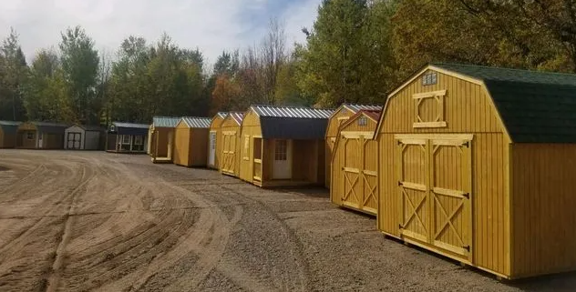 Row of yellow storage sheds on a gravel lot, various sizes and styles, under a cloudy sky.