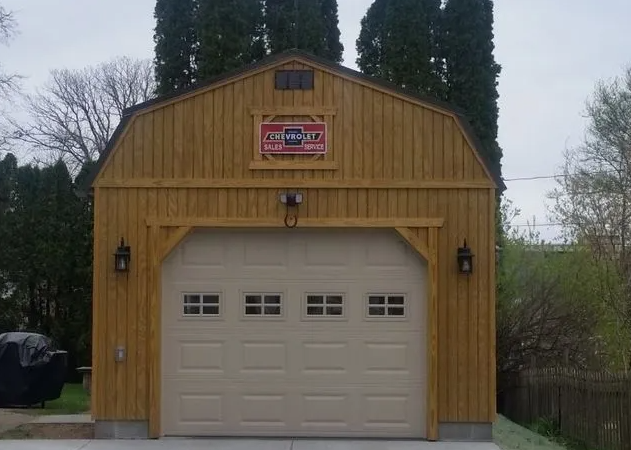 Tan barn-style garage with beige door, black lanterns, and a red sign. Trees frame the building.