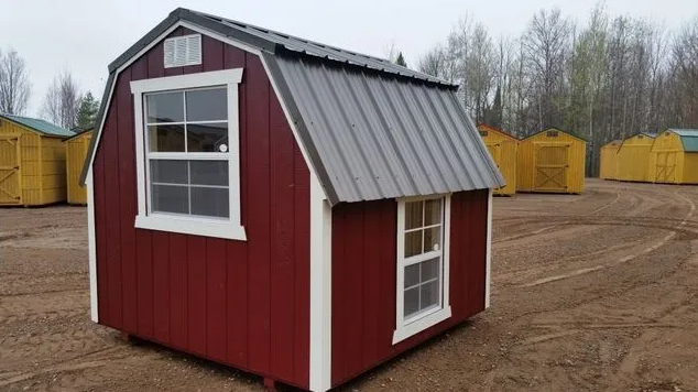 Red storage shed with white trim, grey roof, and two windows; several yellow sheds are in the background.