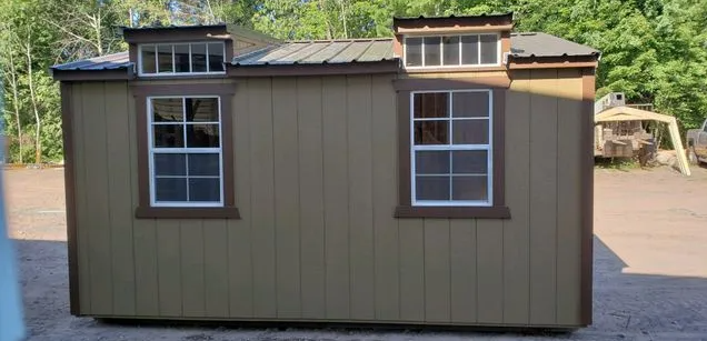 A small, light brown shed with two windows, two smaller windows above, and a dark metal roof.
