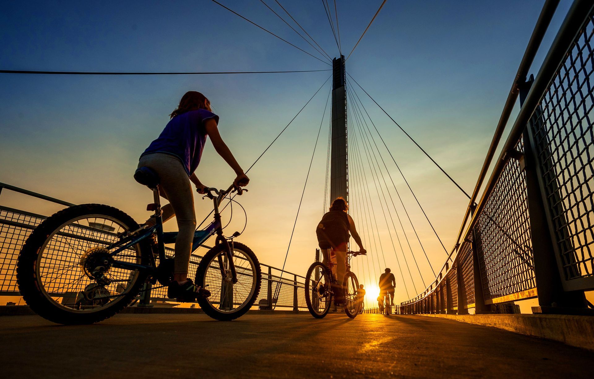 Cyclists riding on a bridge at sunset, silhouetted against a golden sky