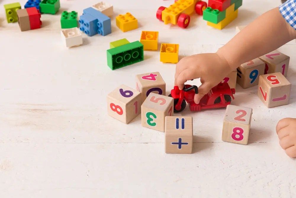 Child’s hand playing with colorful number blocks and toy cars on a white table