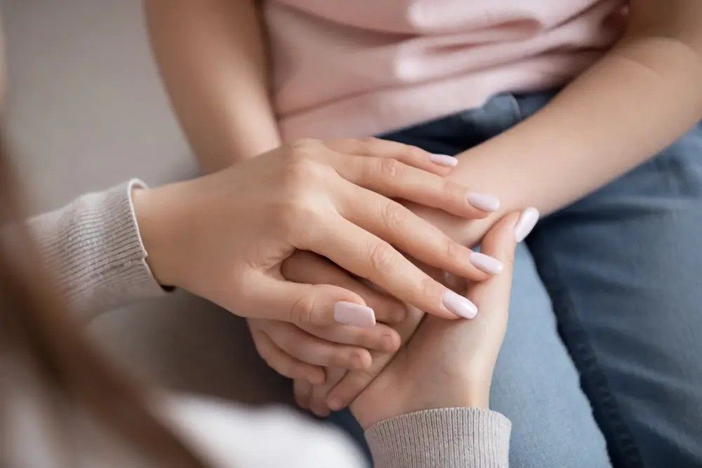 Two hands gently holding another person’s hand on a lap, conveying comfort and support.