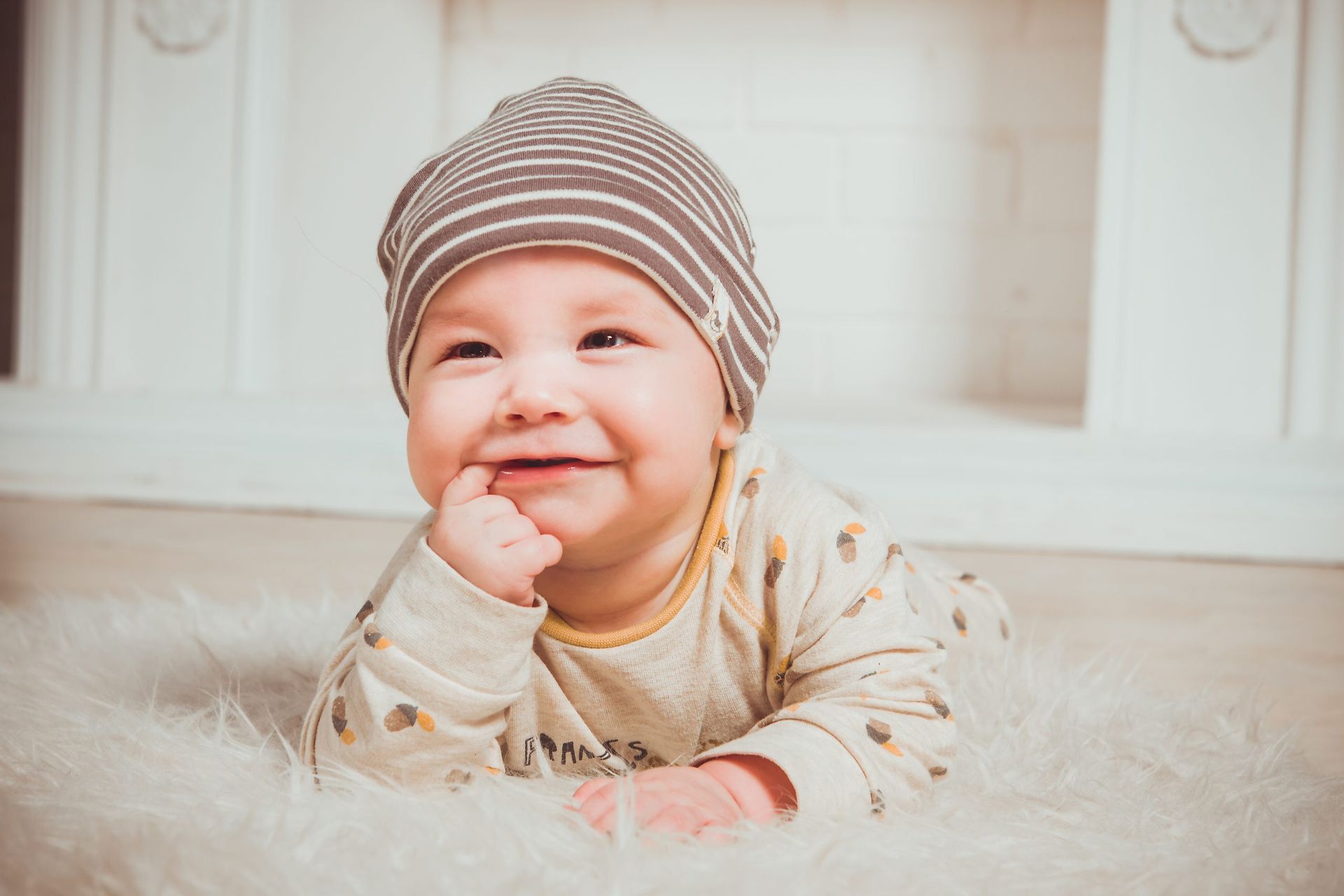 Smiling baby in a striped hat лежing on a soft rug indoors