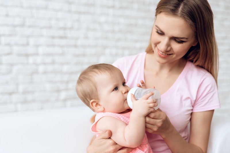 Woman feeding a baby with a bottle on a white couch