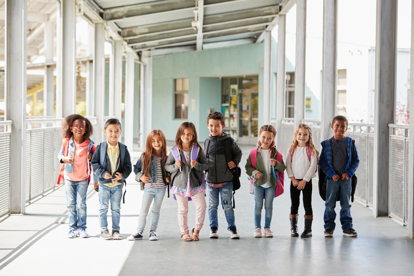 A group of children walking through a bright covered hallway toward the camera.