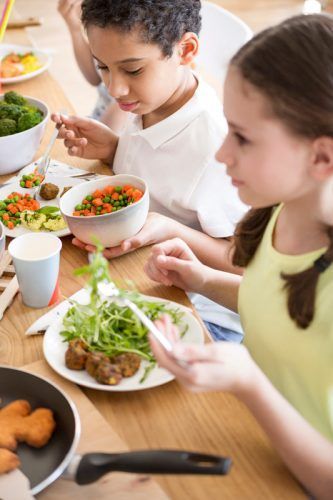 Children eating salad at a table with bowls of vegetables and utensils