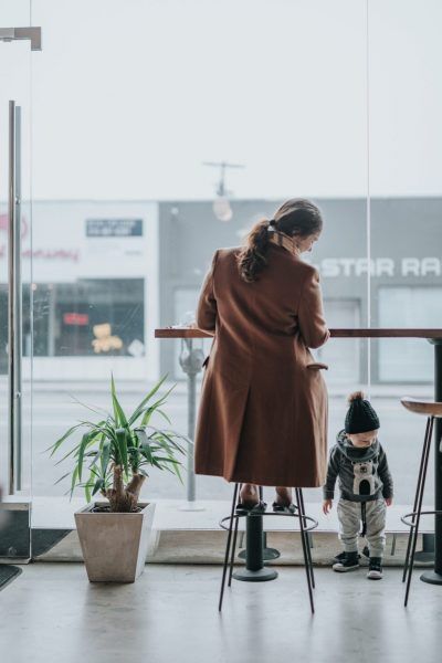 Adult and child by a window in a café, with stools and a potted plant nearby