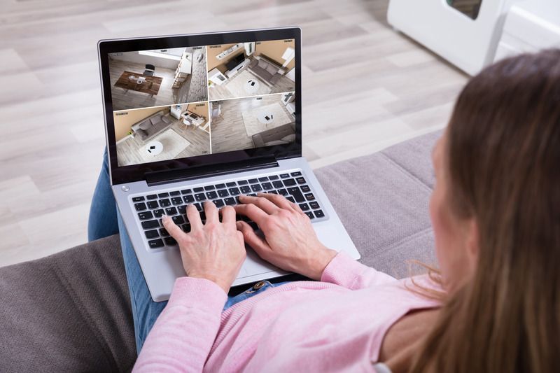 Person typing on a laptop showing multiple security camera views from a couch.