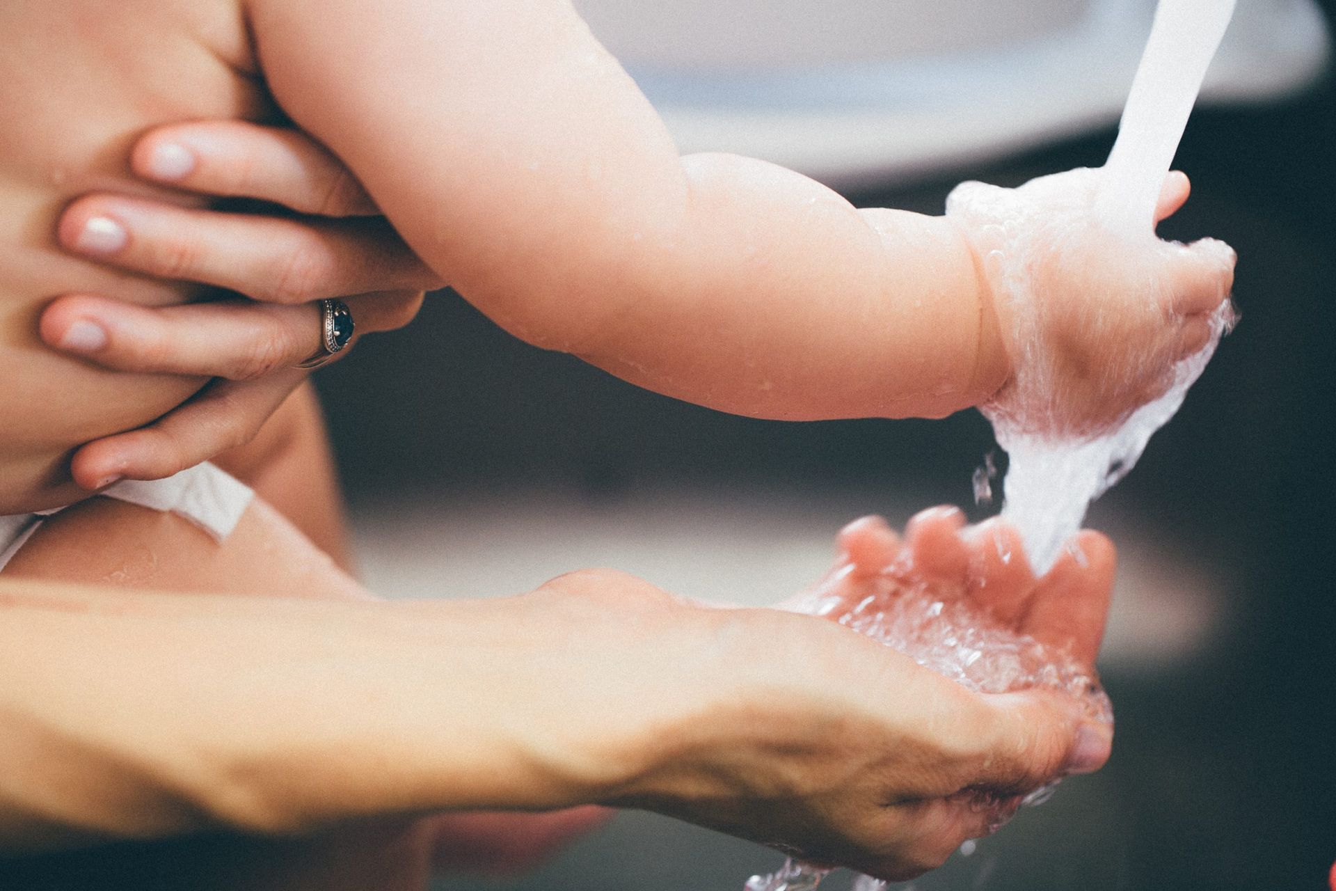 Child’s hands being washed with water by an adult’s hands over a sink