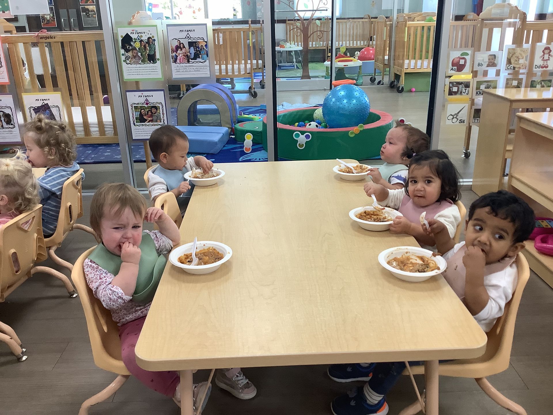 Children seated around a table eating bowls of food in a daycare classroom