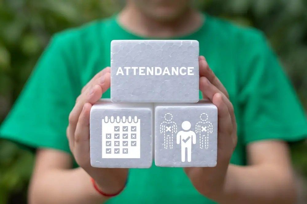 Person holding blocks labeled “ATTENDANCE” with calendar and employee icons, green shirt background