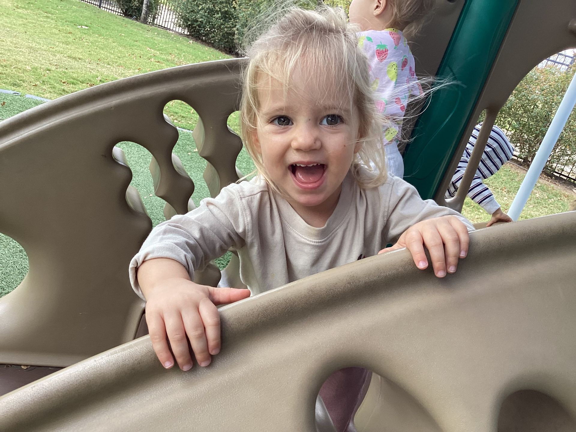 Smiling child on a playground climbing structure, holding the railing and looking at the camera.