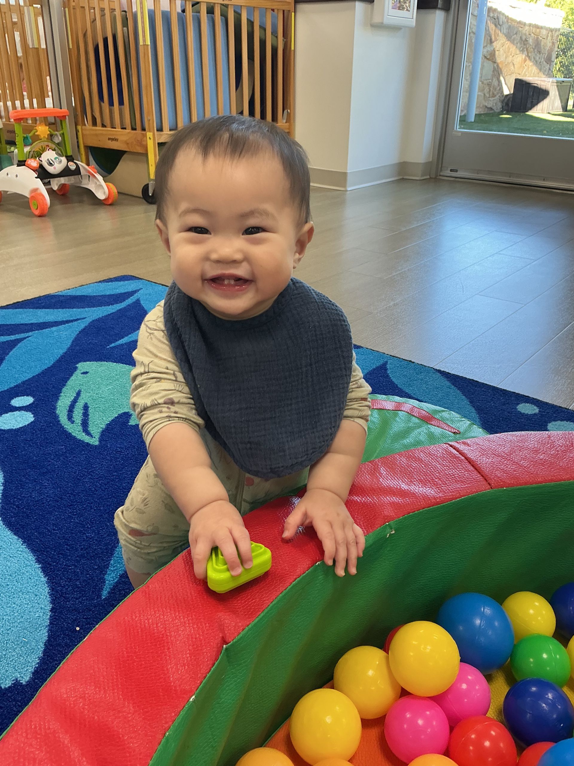Smiling baby playing with colorful balls on a blue rug indoors