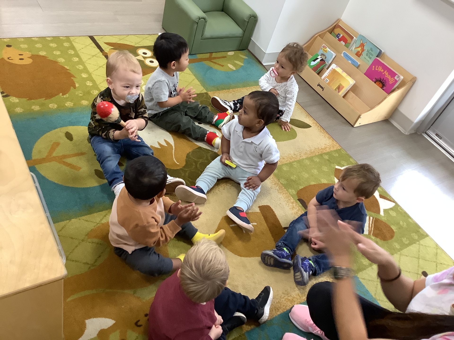 Children sitting in a circle on a colorful classroom rug, playing together with toys.