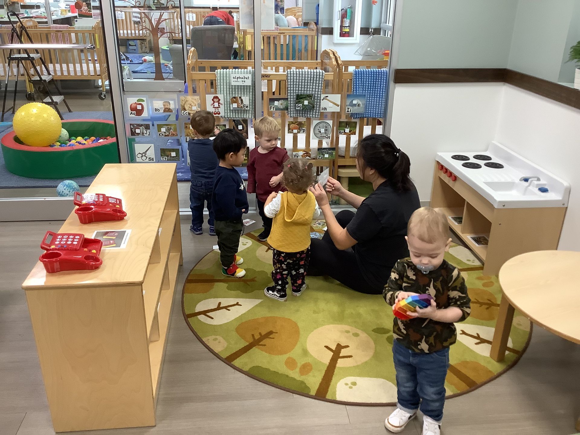 Children playing in a daycare corner with toys and a caregiver on a circular rug