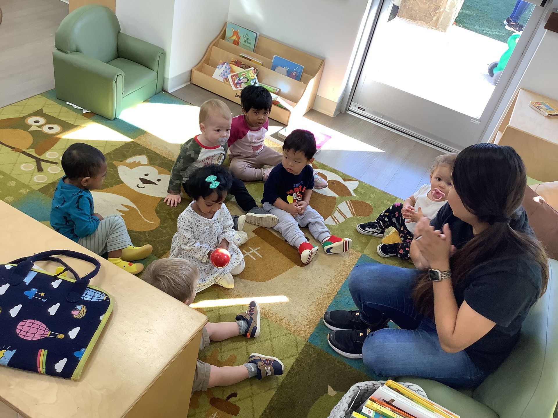 Adult sitting with several children in a classroom, engaging in a group activity on the floor.