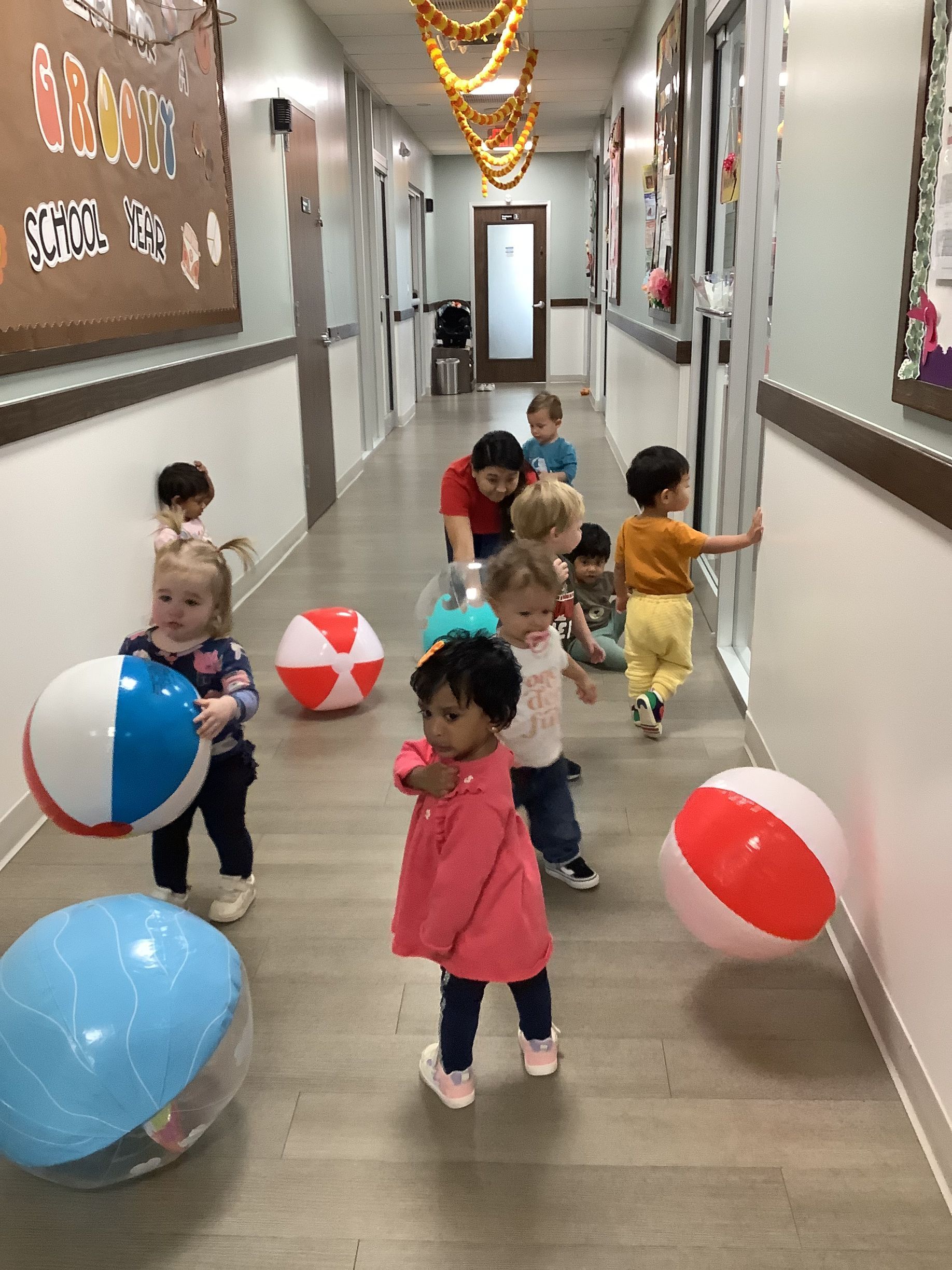 Children running in a school hallway, surrounded by large red, blue, and white balls.