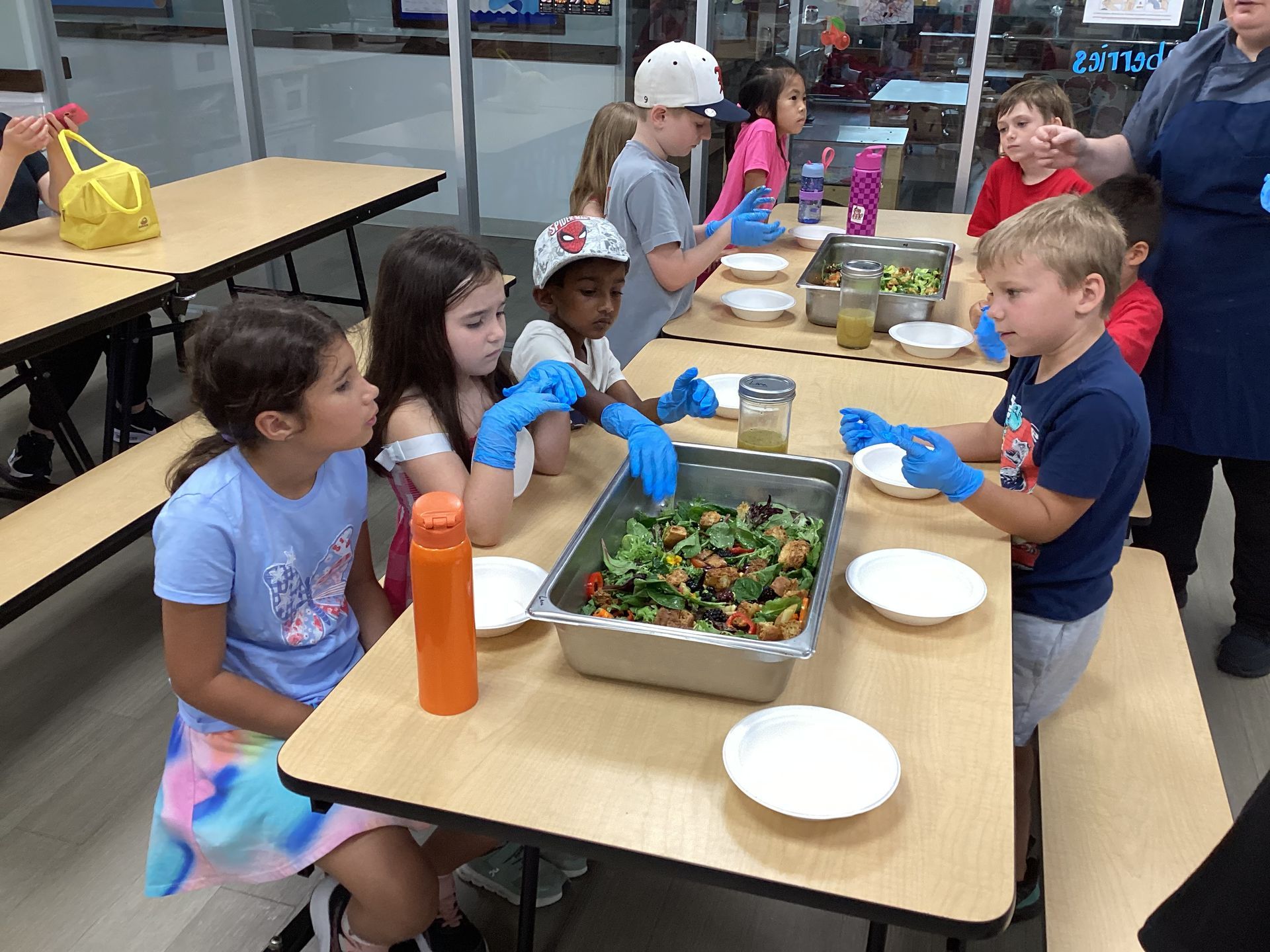 Children eating lunch around a table with trays and water bottles in a cafeteria