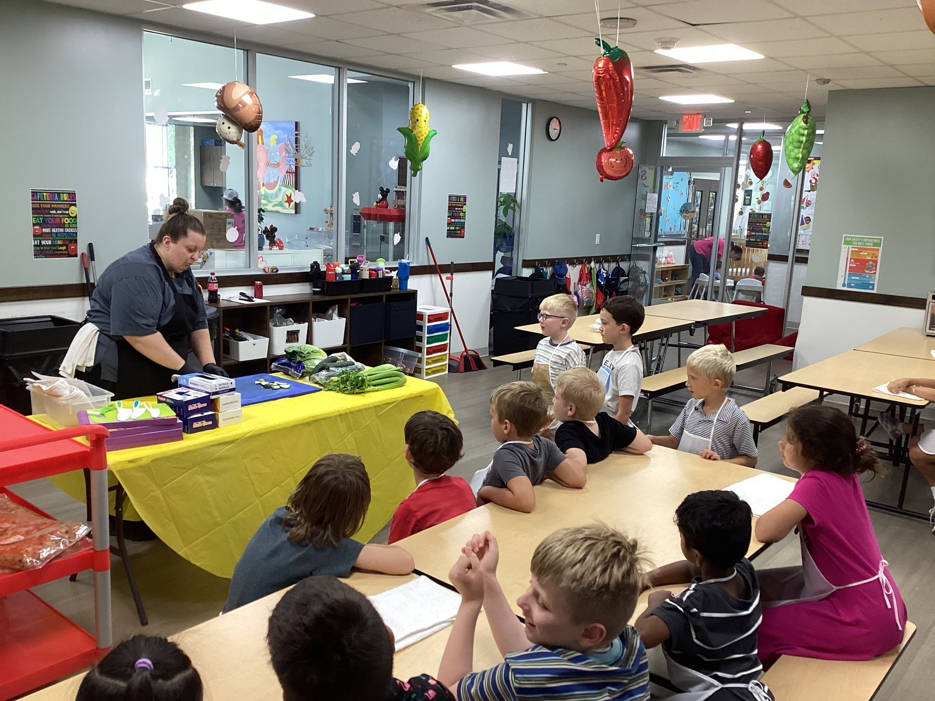 Children sitting on a floor listen to a presenter at a decorated classroom party table.