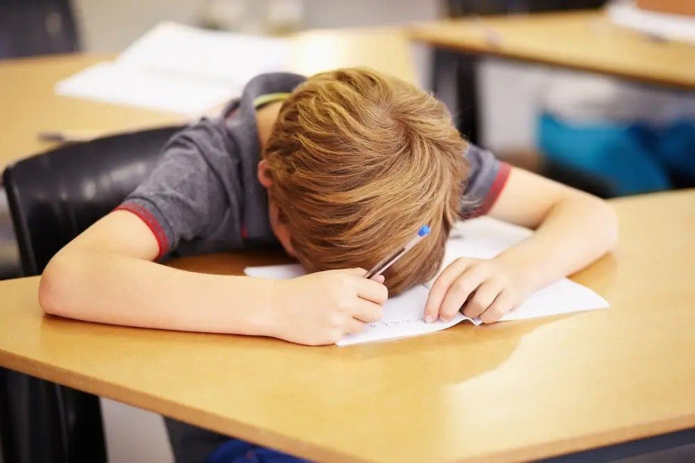 Boy writing with head down at a classroom desk