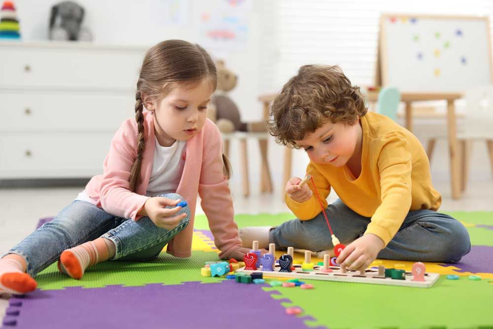 Two children playing with colorful blocks on a foam mat in a bright playroom