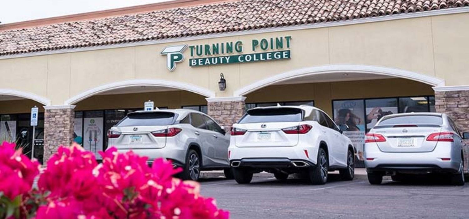 Turning Point Beauty College building with cars parked out front, pink flowers in the foreground.