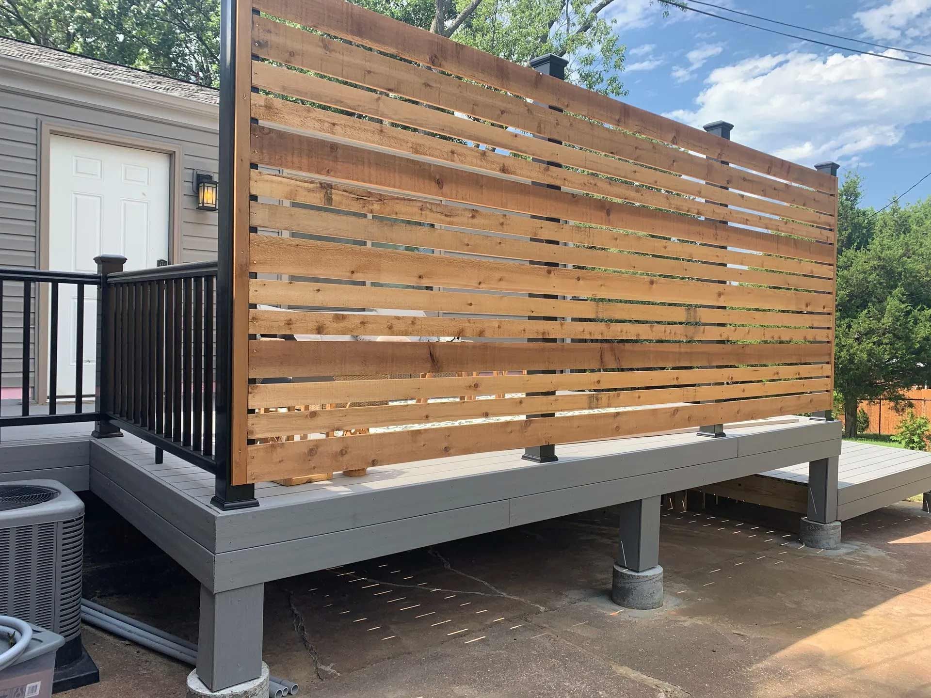 A wooden fence surrounds a deck with a black railing.