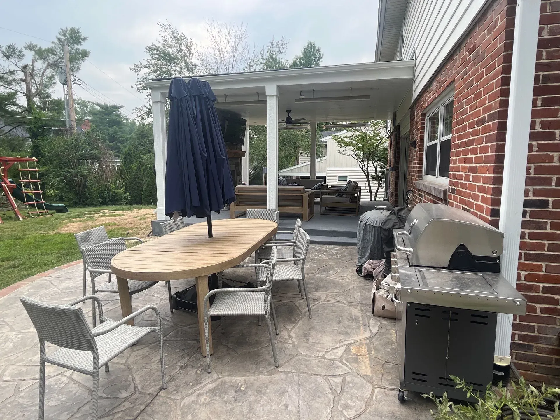 A patio with a table, chair, umbrella and grill.