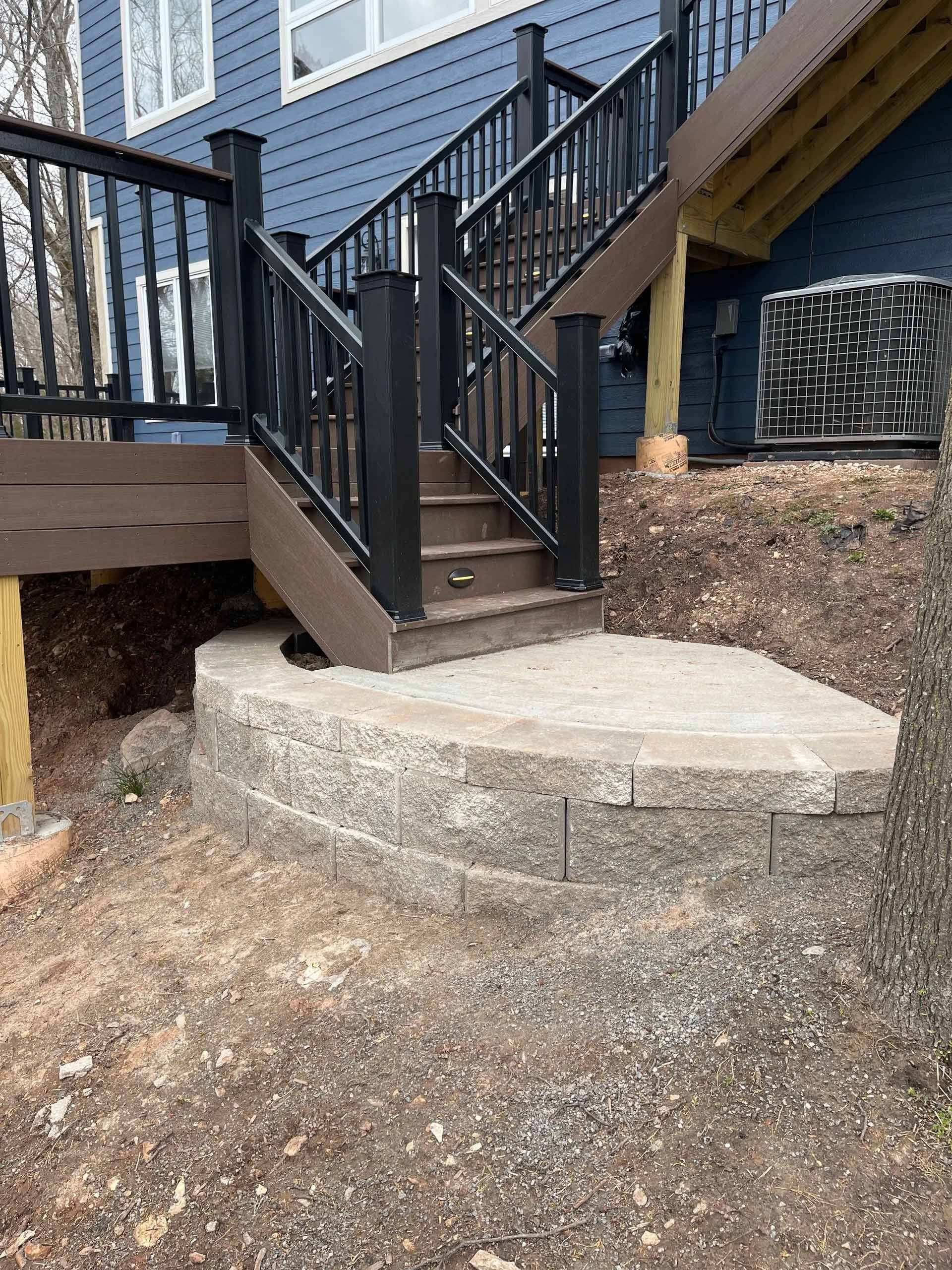 A deck with stairs leading up to it and a blue house in the background.