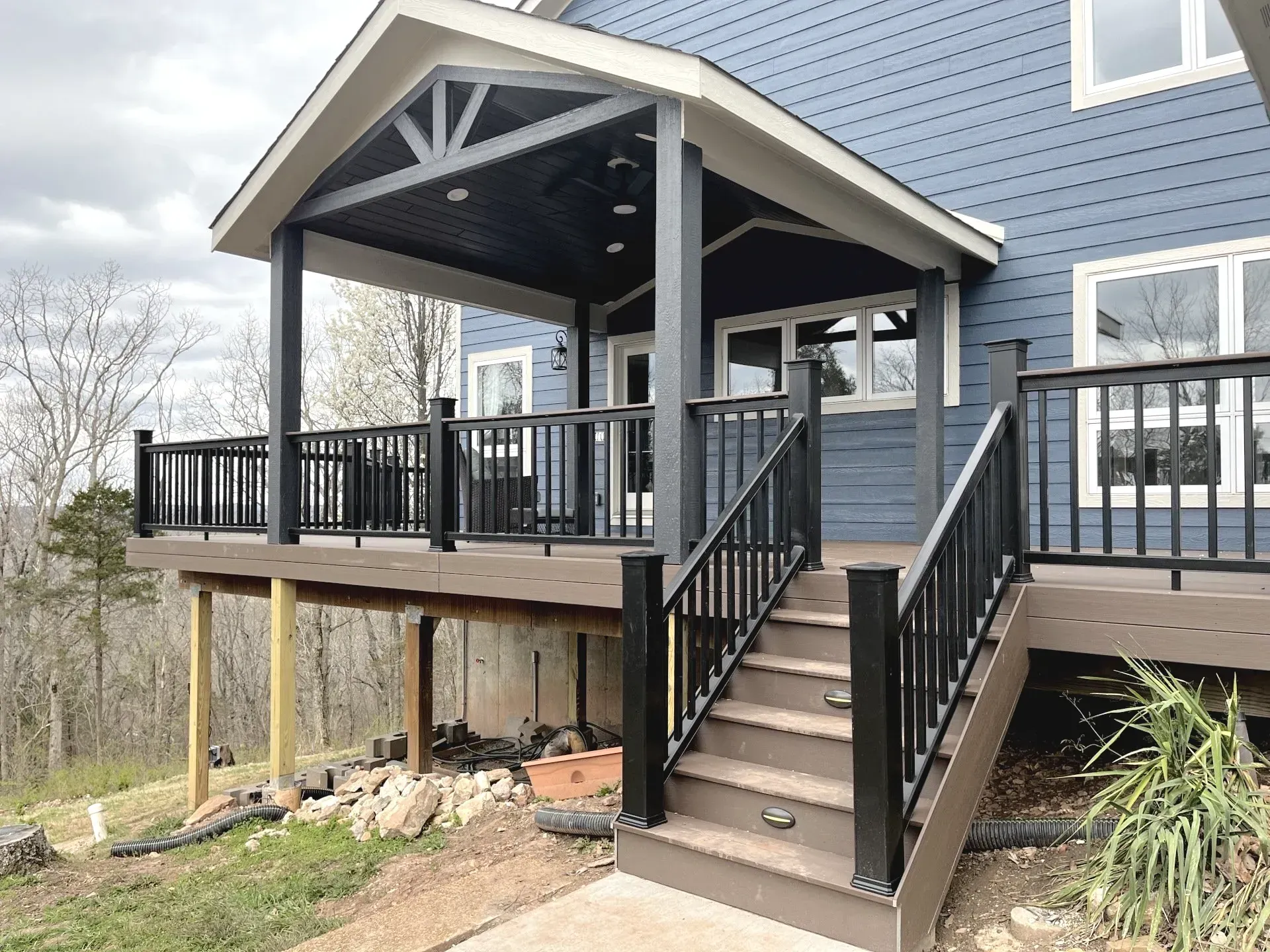 A blue house with a large deck and stairs leading up to it.